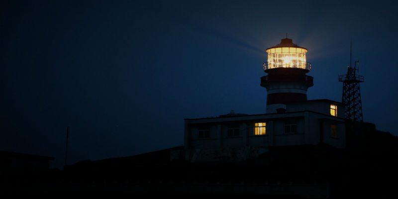 A lighthouse during night, only silhouette of the lighthouse can be seen and the lights.